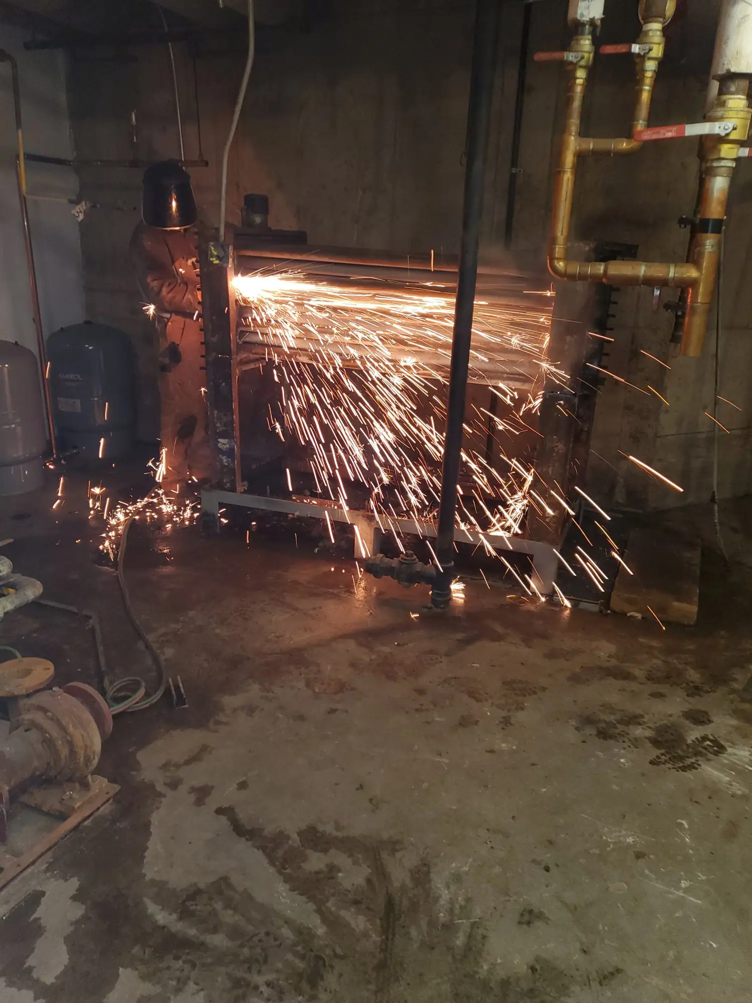 Torch cutting a boiler in a basement mechanical room, sparks flying