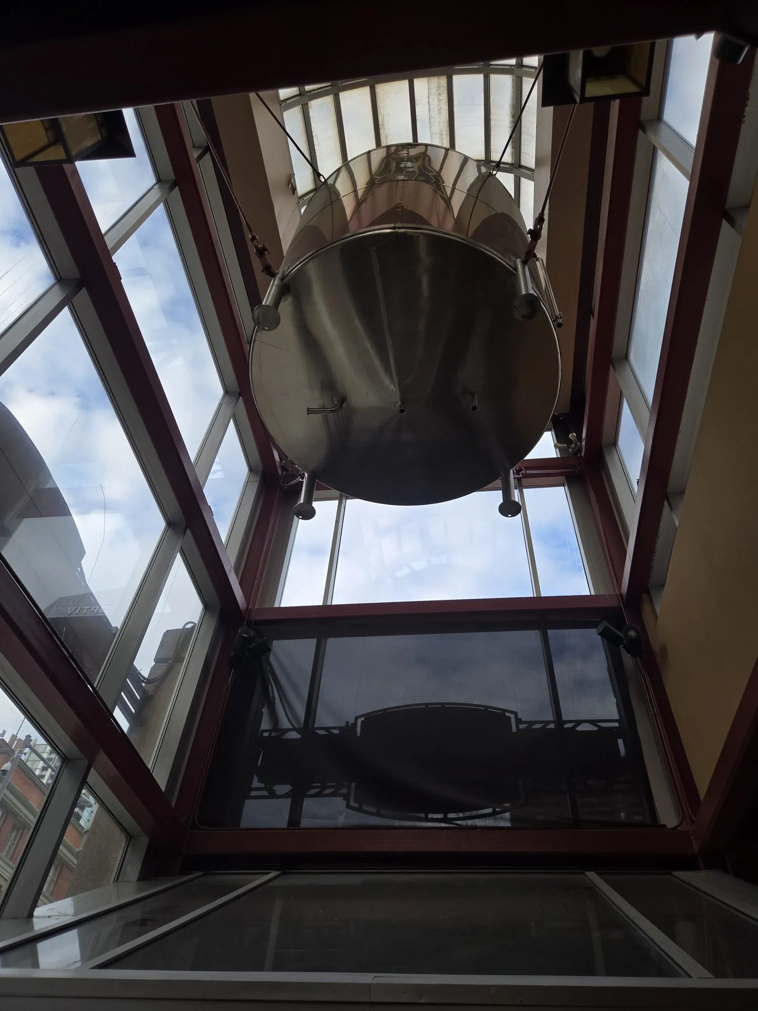 Stainless steel process vessel suspended 24 feet up in a glass atrium before removal