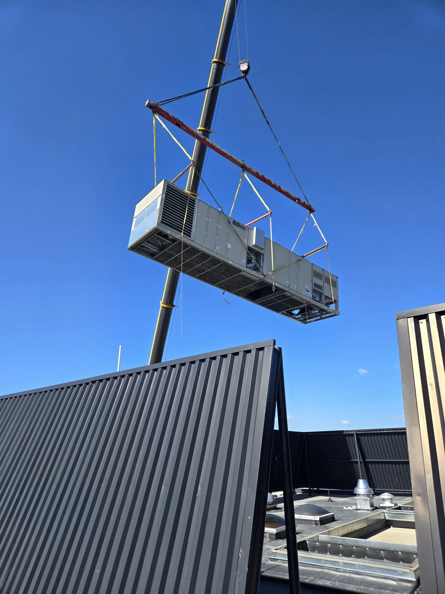 Rooftop air handling unit lifted by crane against a blue sky